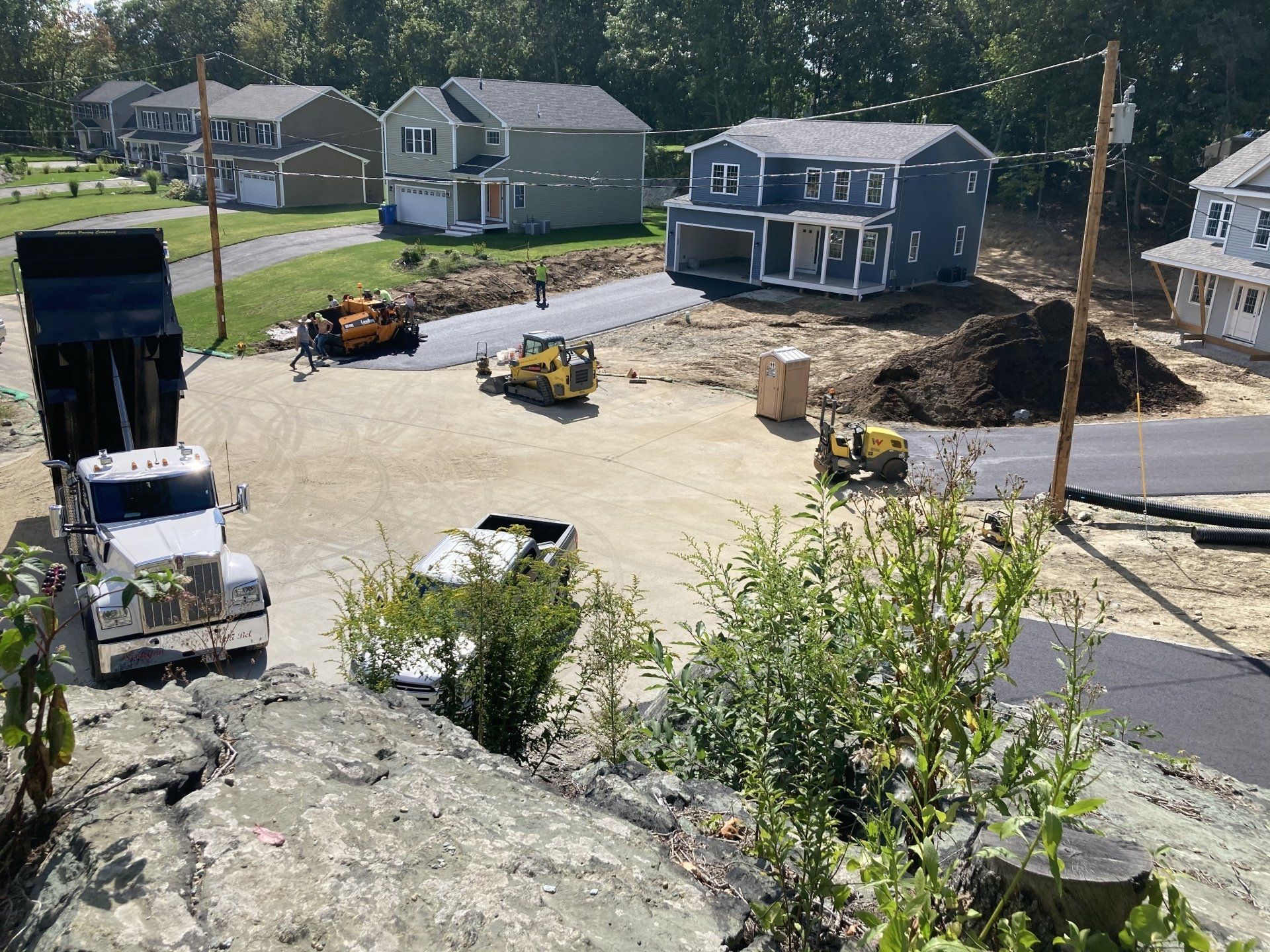 A dump truck is driving down a dirt road in a residential area