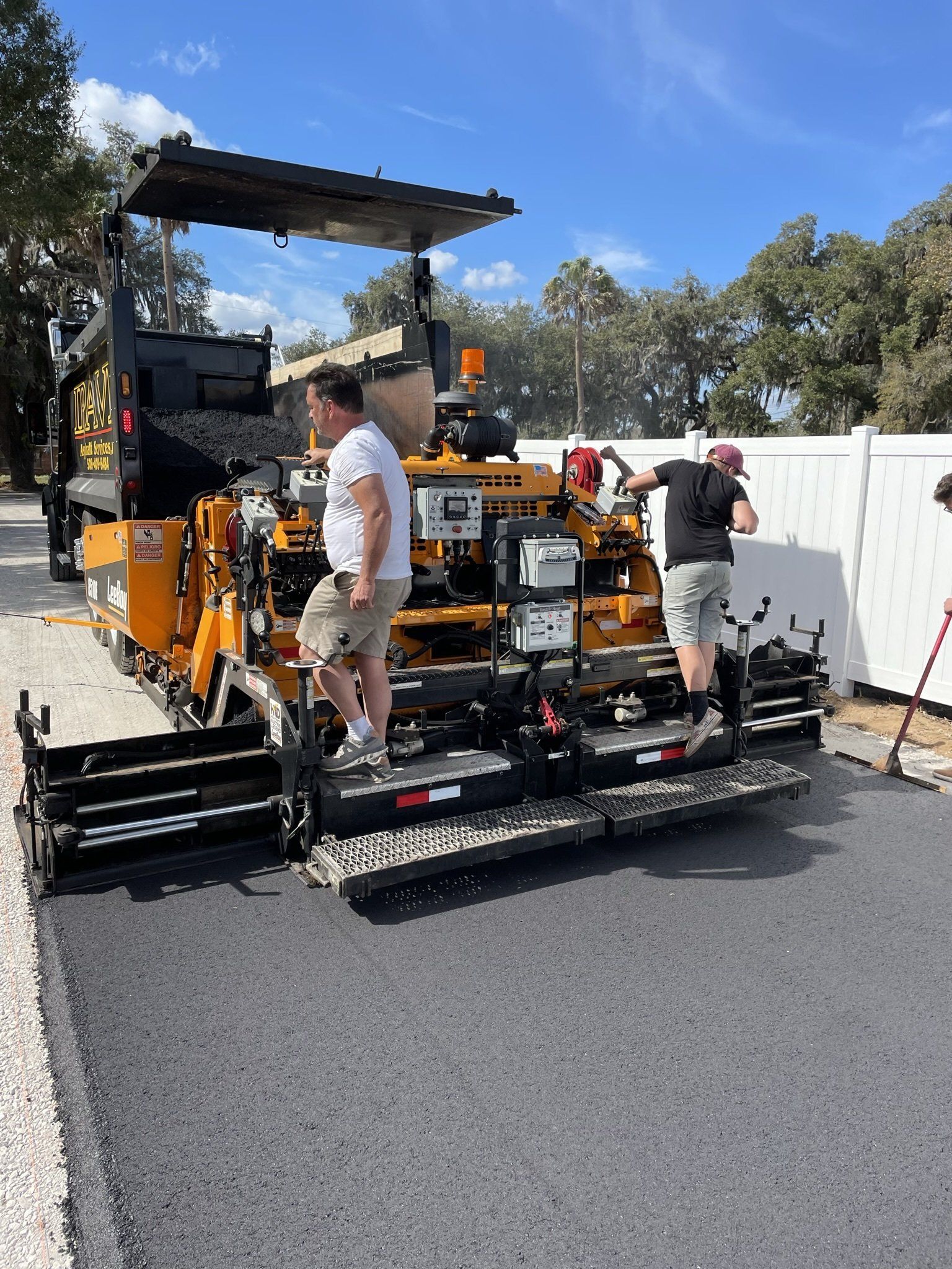 A man is standing next to a machine that is laying asphalt on a road.