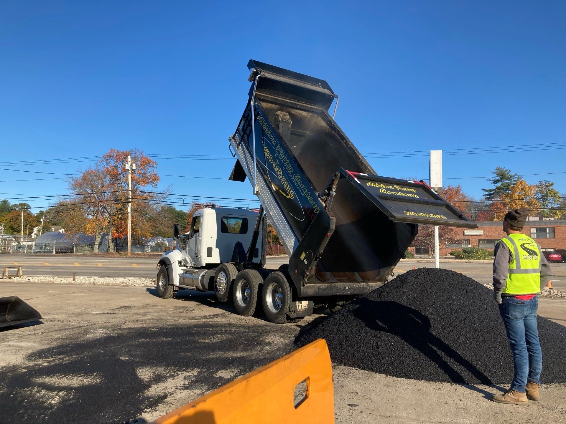 A man in a yellow vest is standing next to a dump truck.