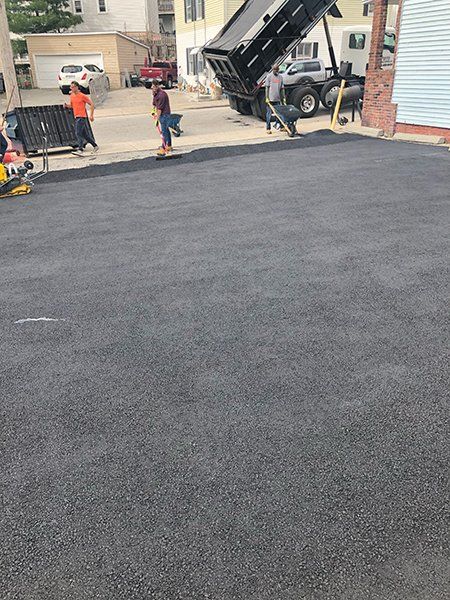 A dump truck is being loaded with asphalt in a driveway.
