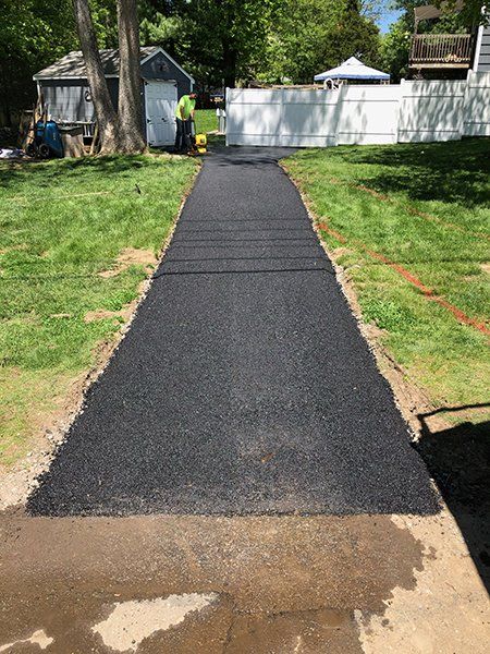 A man is standing on a sidewalk next to a grassy field.