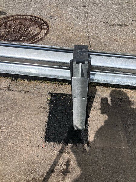 A metal pole is sitting on the side of a road next to a manhole cover.