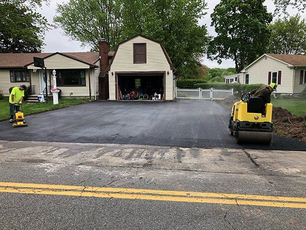 A man is using a vacuum cleaner to clean a driveway in front of a house.