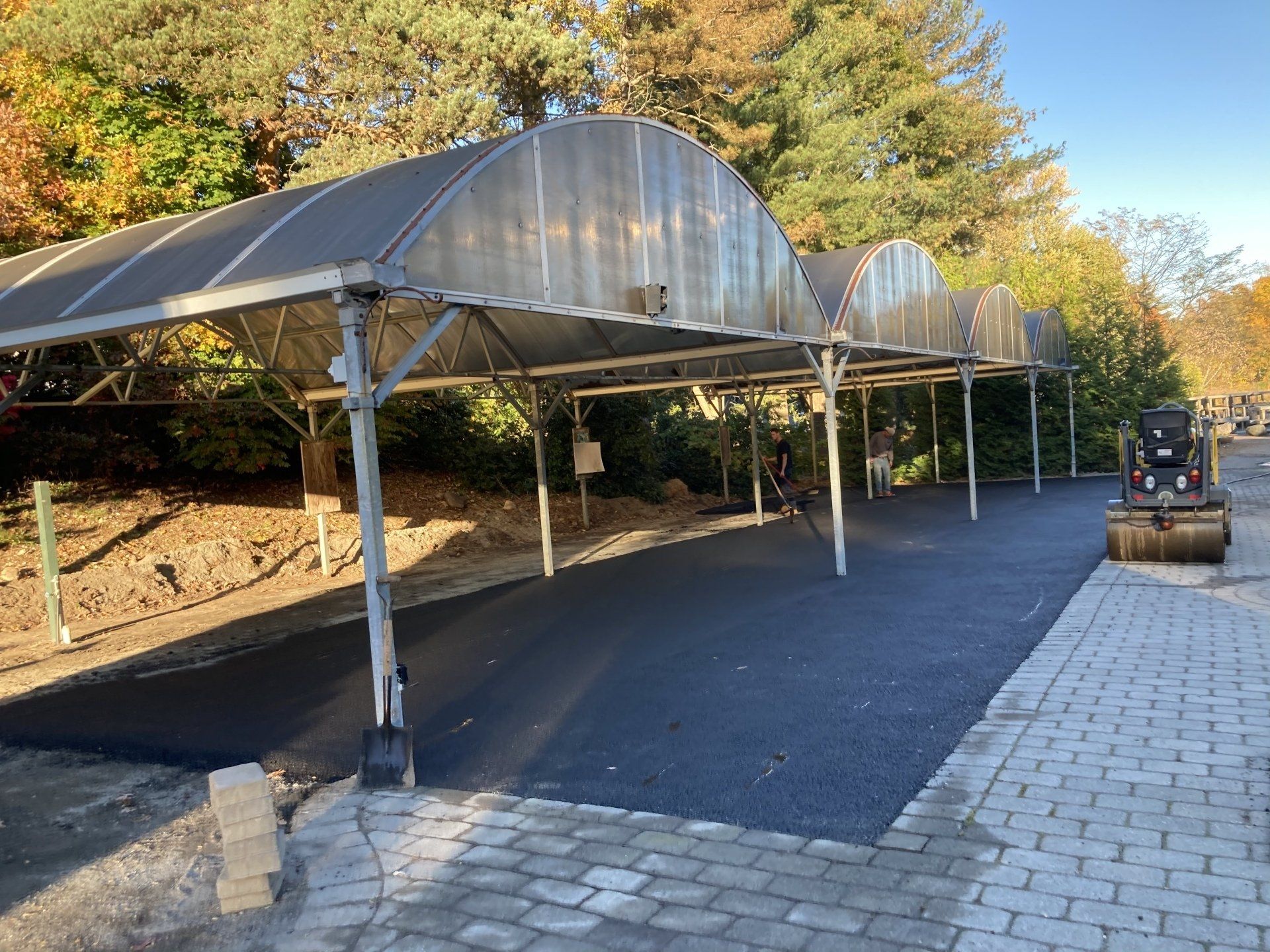 A carport with a clear roof is being built on a brick sidewalk.