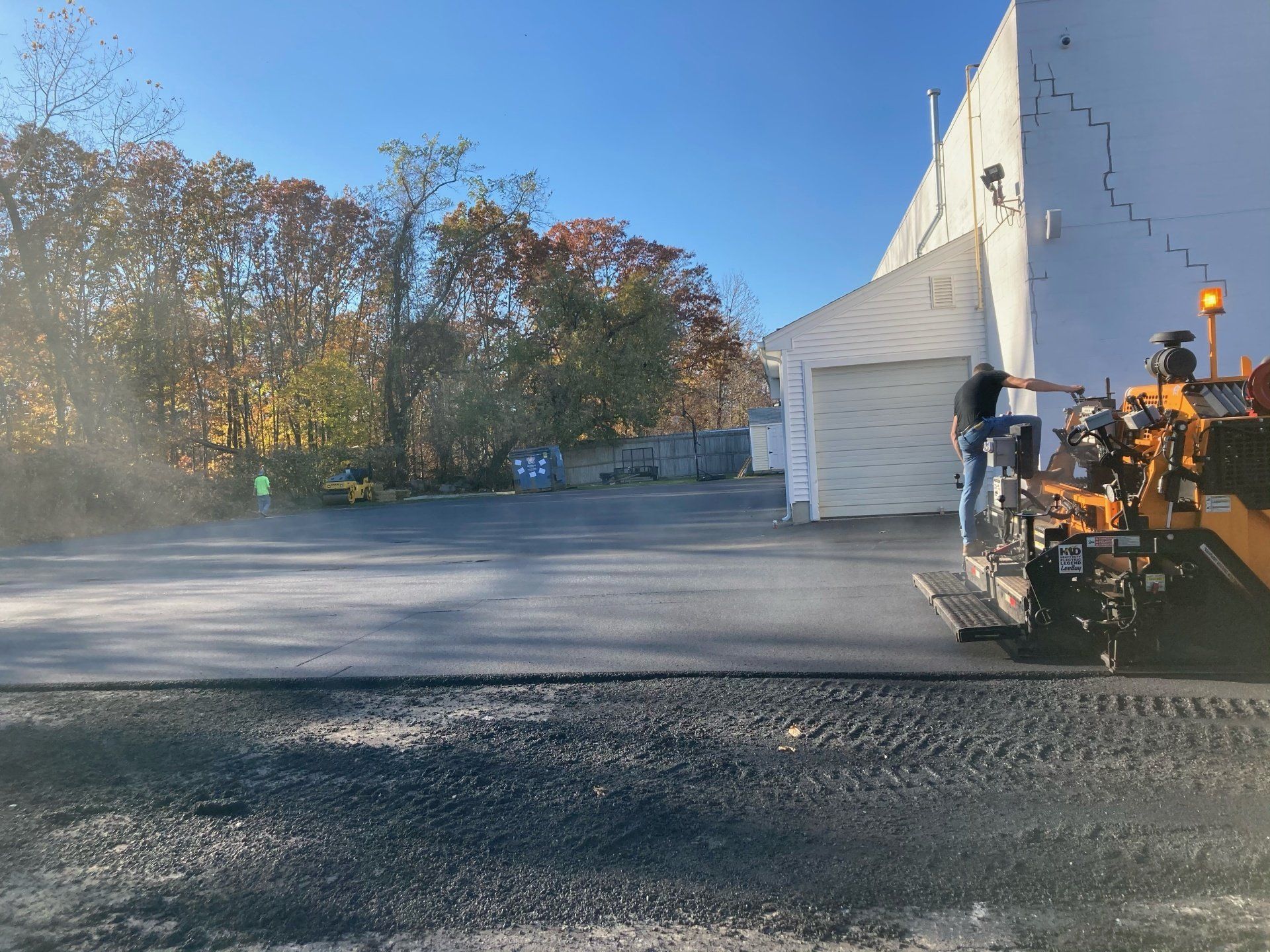 A machine is laying asphalt in a parking lot in front of a building.