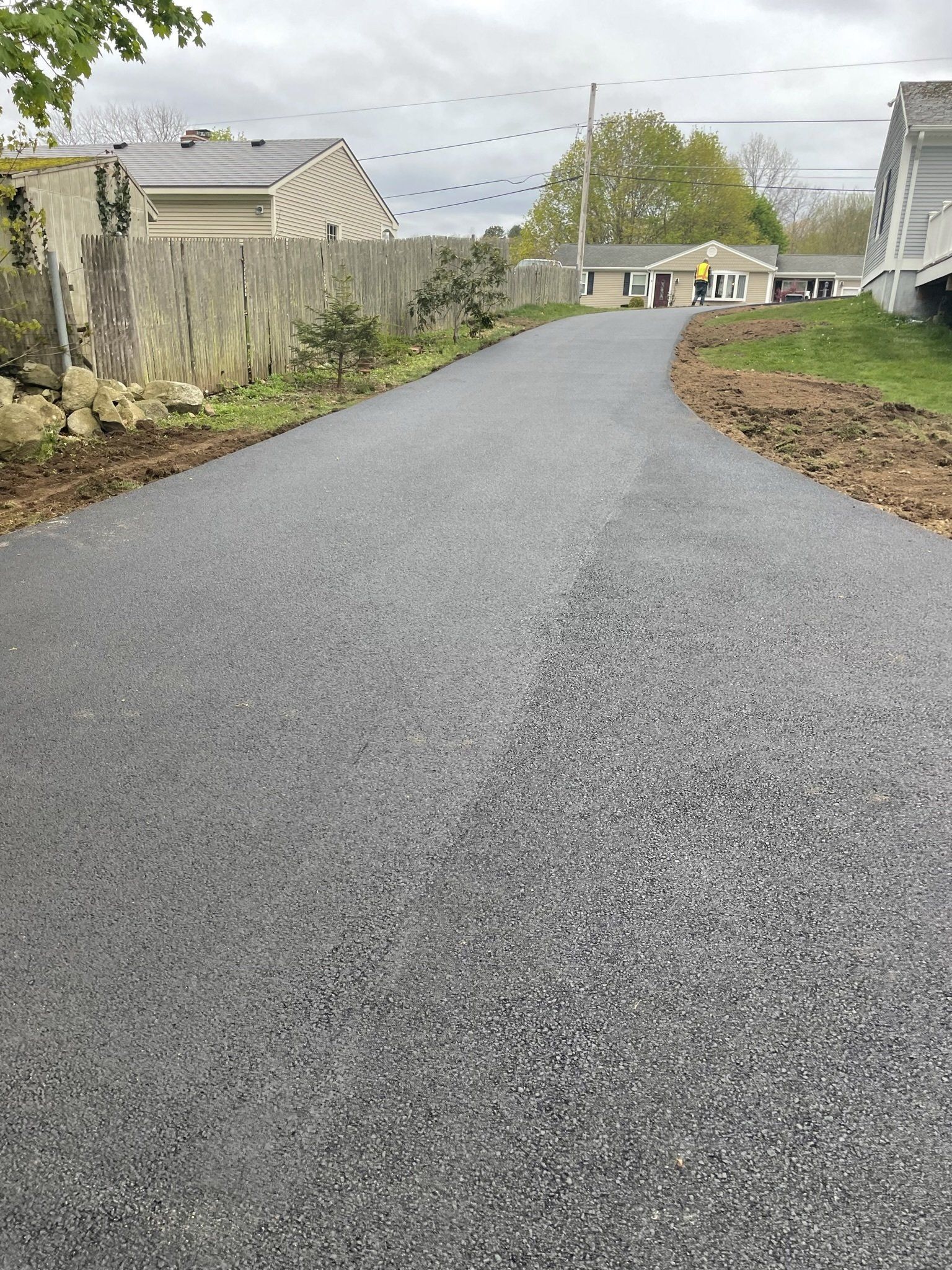 A road with a fence on the side of it and a house in the background.