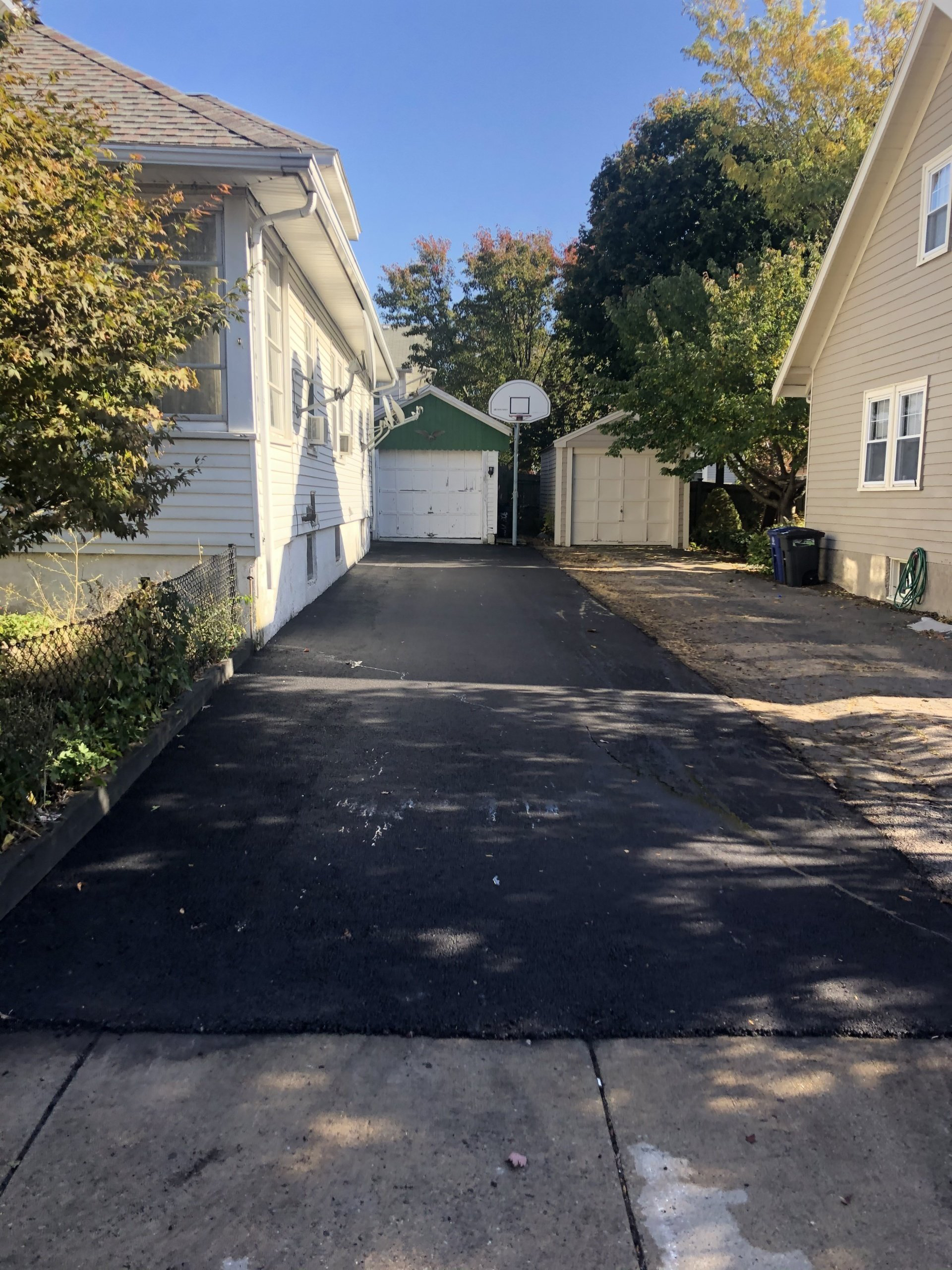 A driveway leading to a house with a basketball hoop in the background