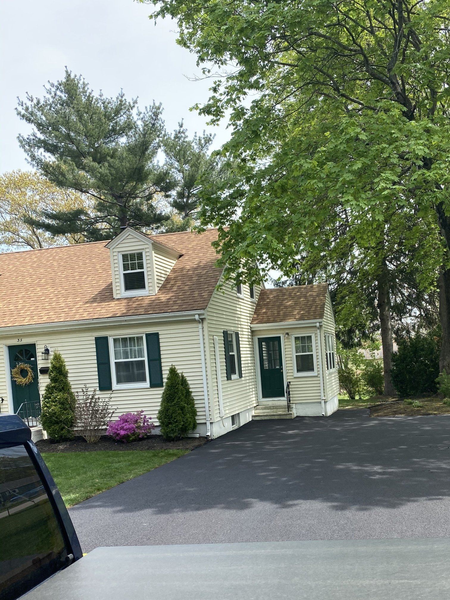 A white house with a brown roof and green shutters is surrounded by trees.