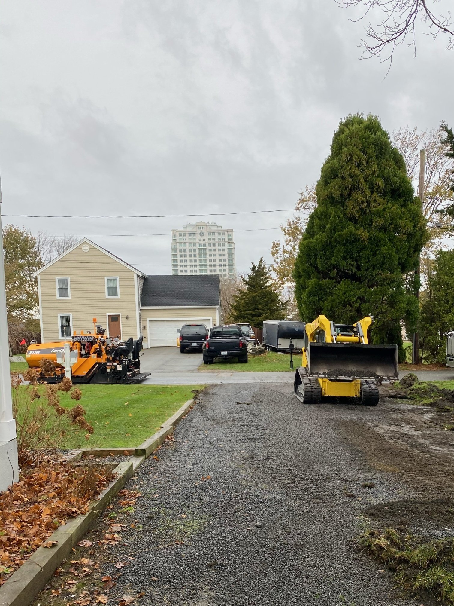 A yellow bulldozer is driving down a gravel driveway in front of a house.