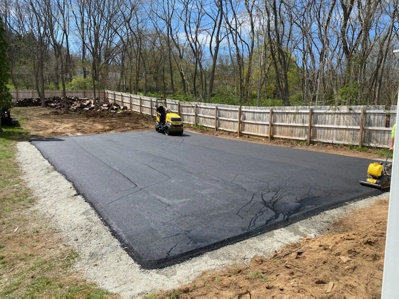 A large asphalt driveway is being built in a backyard.