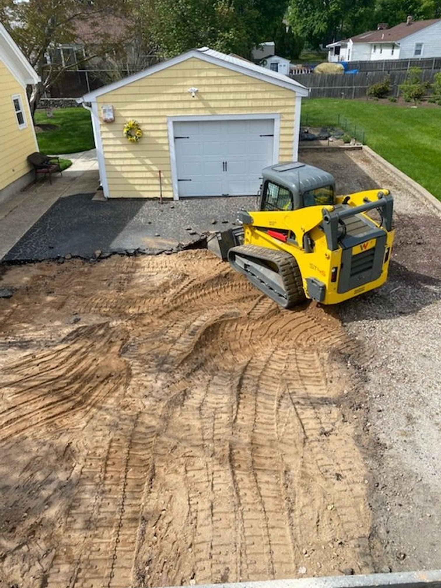 A yellow bulldozer is moving dirt in a driveway in front of a garage.