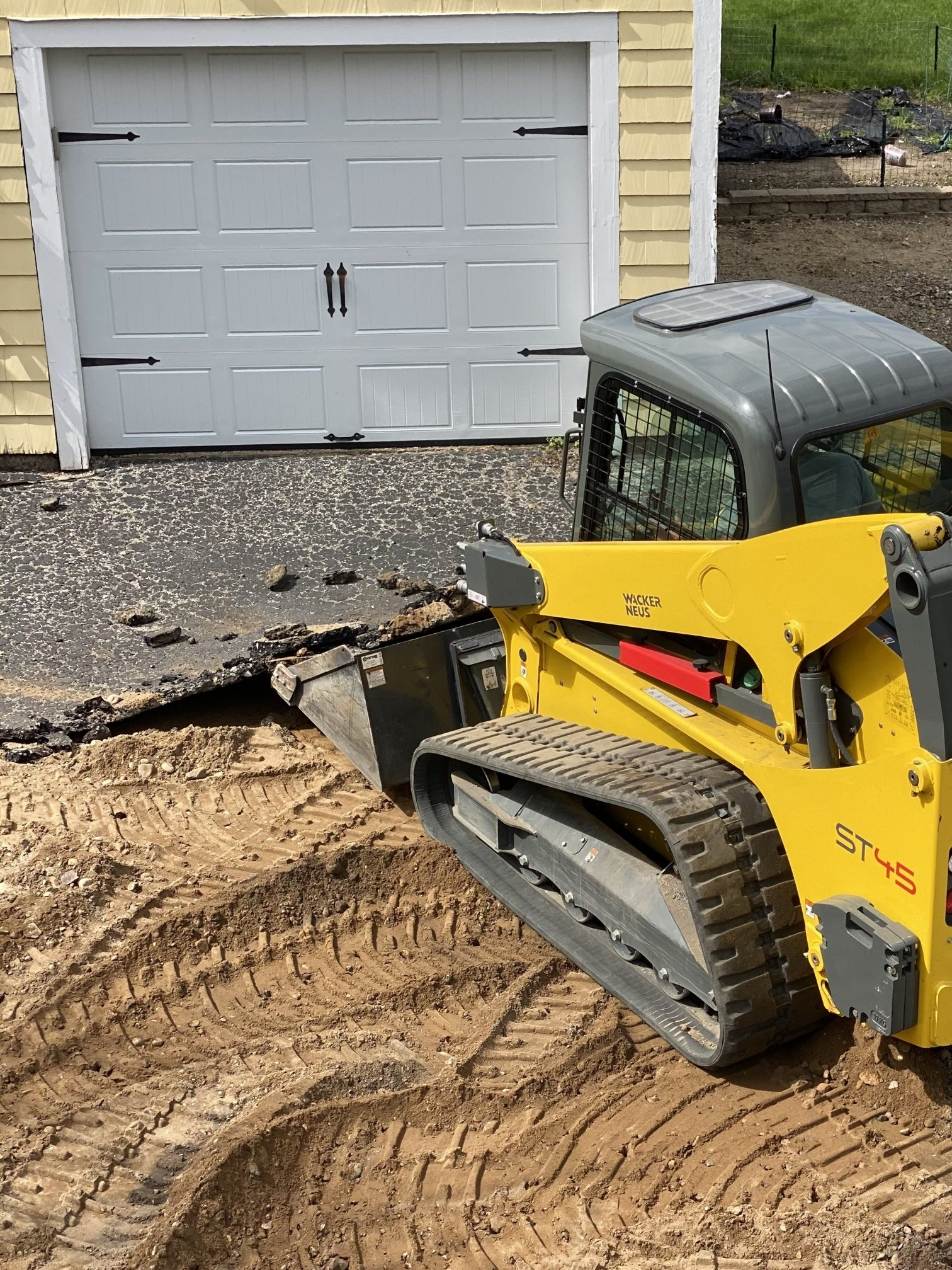 A yellow bulldozer is moving dirt in front of a garage.