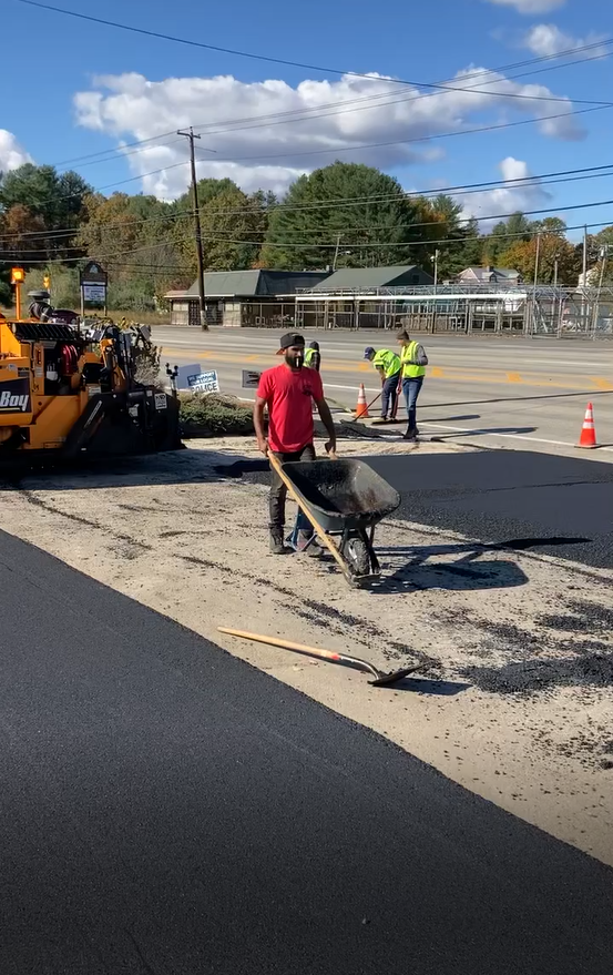 A man is pushing a wheelbarrow down a road.