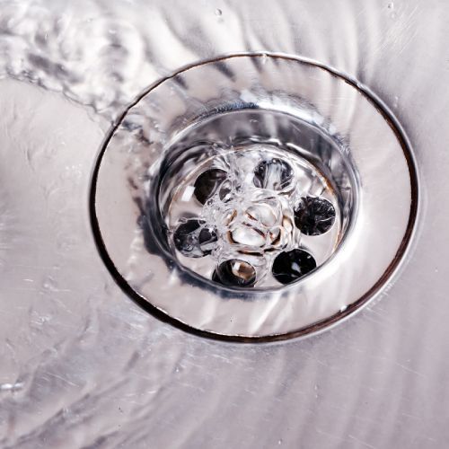 Water flowing into a shiny, chrome sink drain.