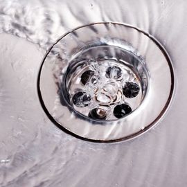 Water flowing into a shiny, chrome sink drain.