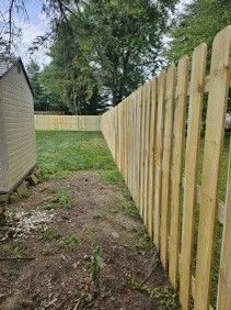 A wooden picket fence surrounds a backyard with a shed in the background.