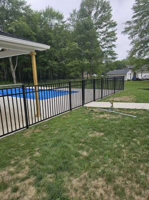 A black fence surrounds a swimming pool in a backyard.