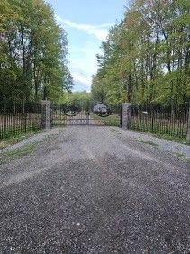 A gravel road leading to a fenced in area with trees on both sides.