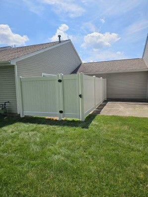 A white vinyl fence with a gate is in the backyard of a house.