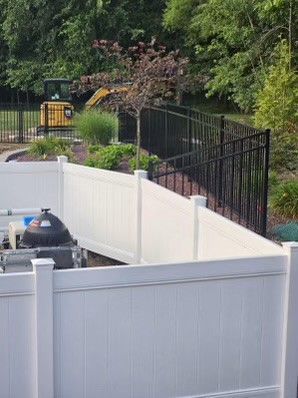 A white fence with a black fence and a bulldozer in the background.