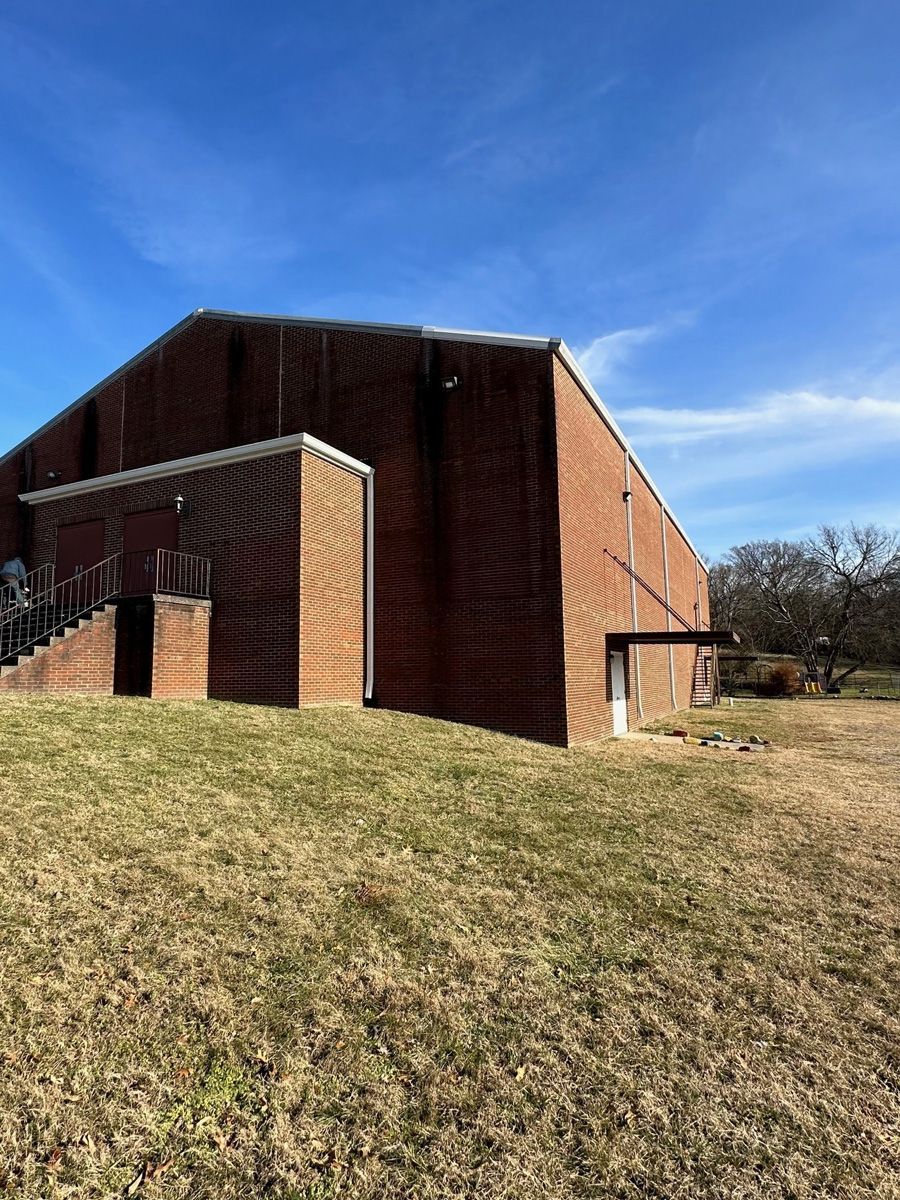 A large brick building is sitting on top of a grassy hill.