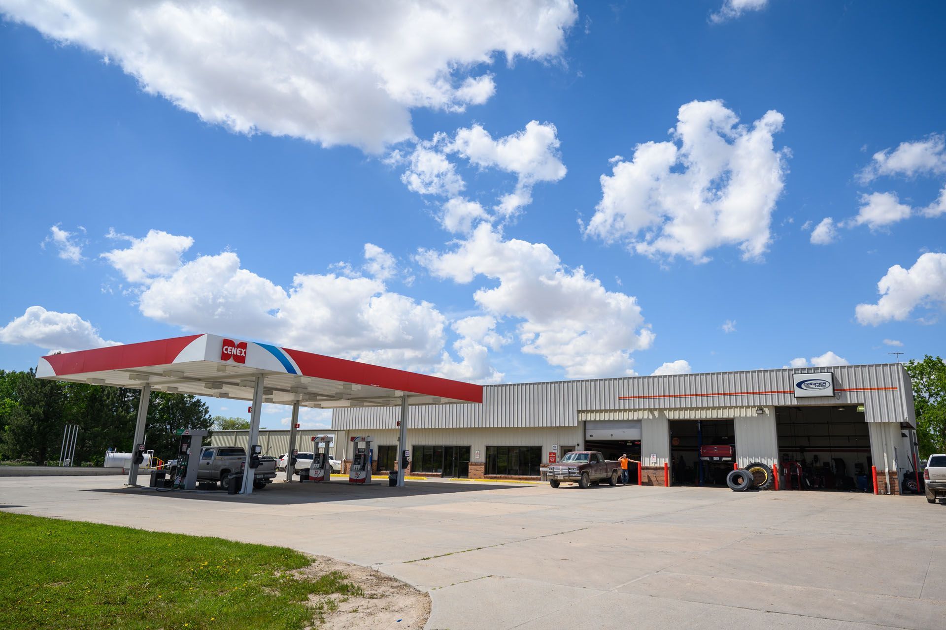 Gas station with red-and-white canopy, parked cars, and a blue sky with scattered clouds