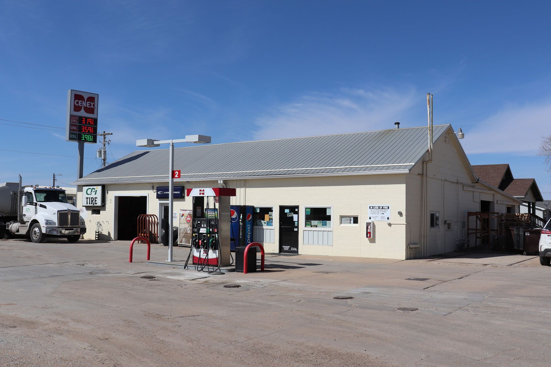 Desert gas station with a white building, fuel pumps, and trucks under a clear blue sky.