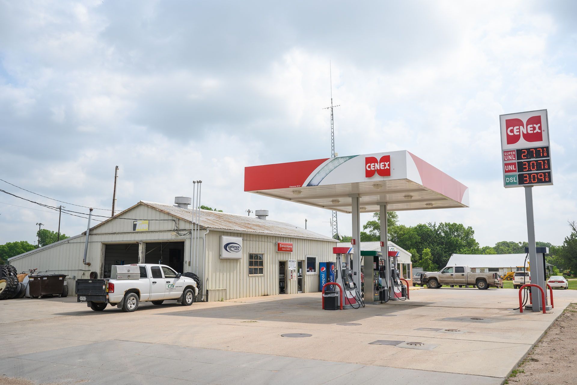 Small gas station with a red-and-white canopy, white truck, and convenience store on a cloudy day