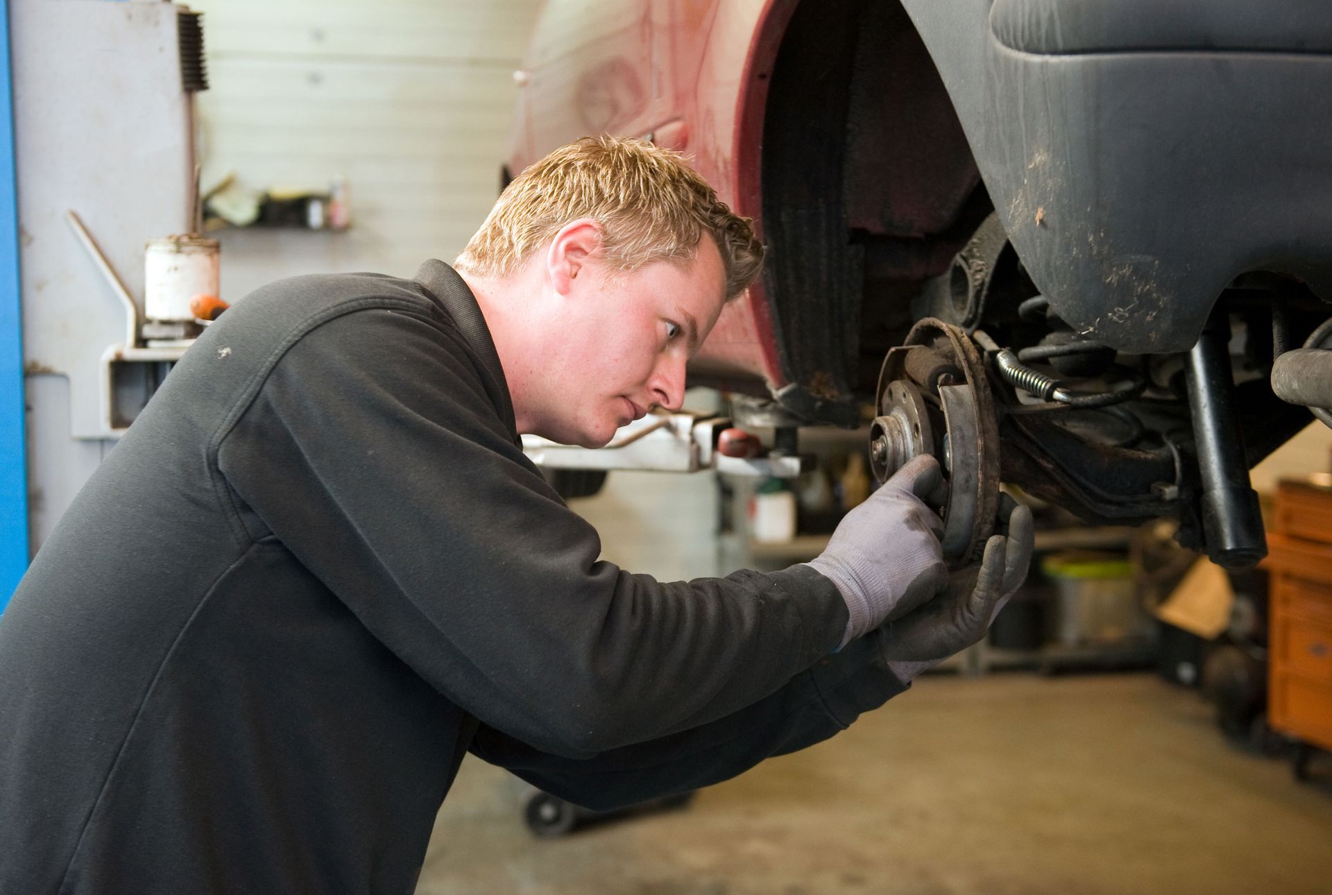 Mechanic using tools to inspect a car’s front wheel in a garage