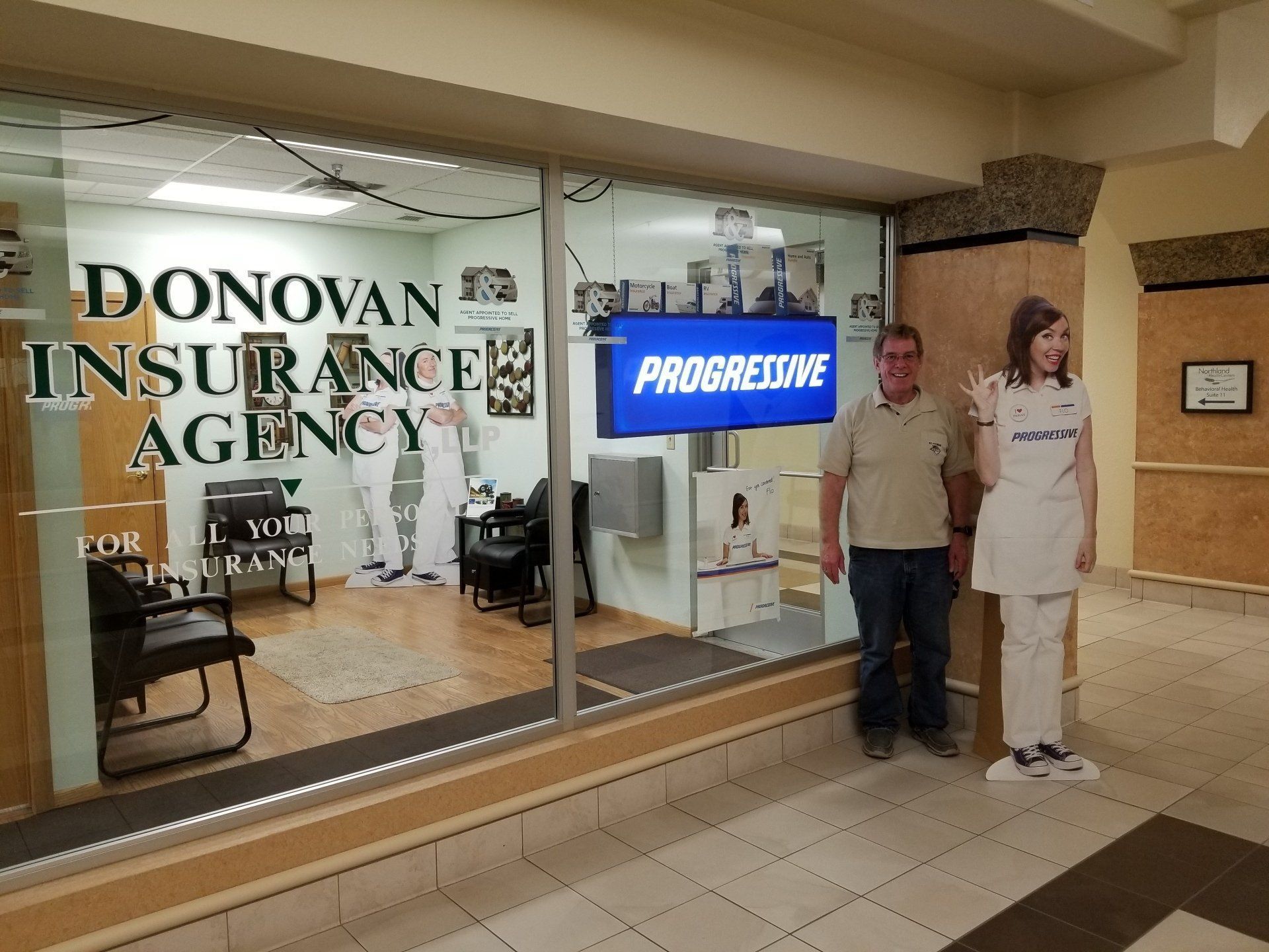 A person stands outside the Donovan Insurance Agency, next to a life-size cutout of the Progressive character, Flo.