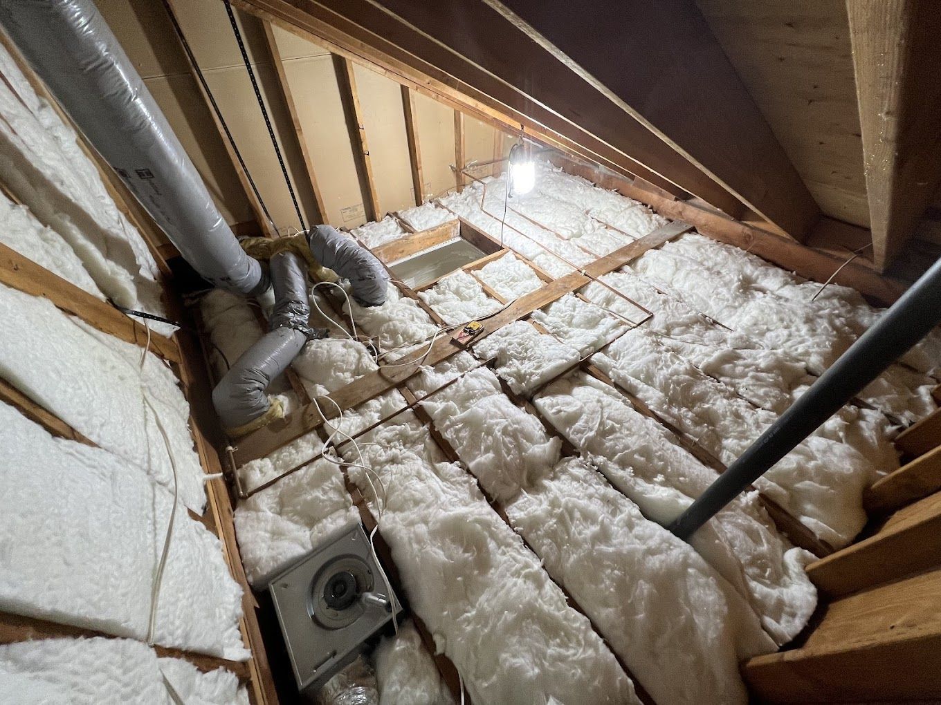 Attic interior with insulation, ventilation, ductwork, and a light fixture.