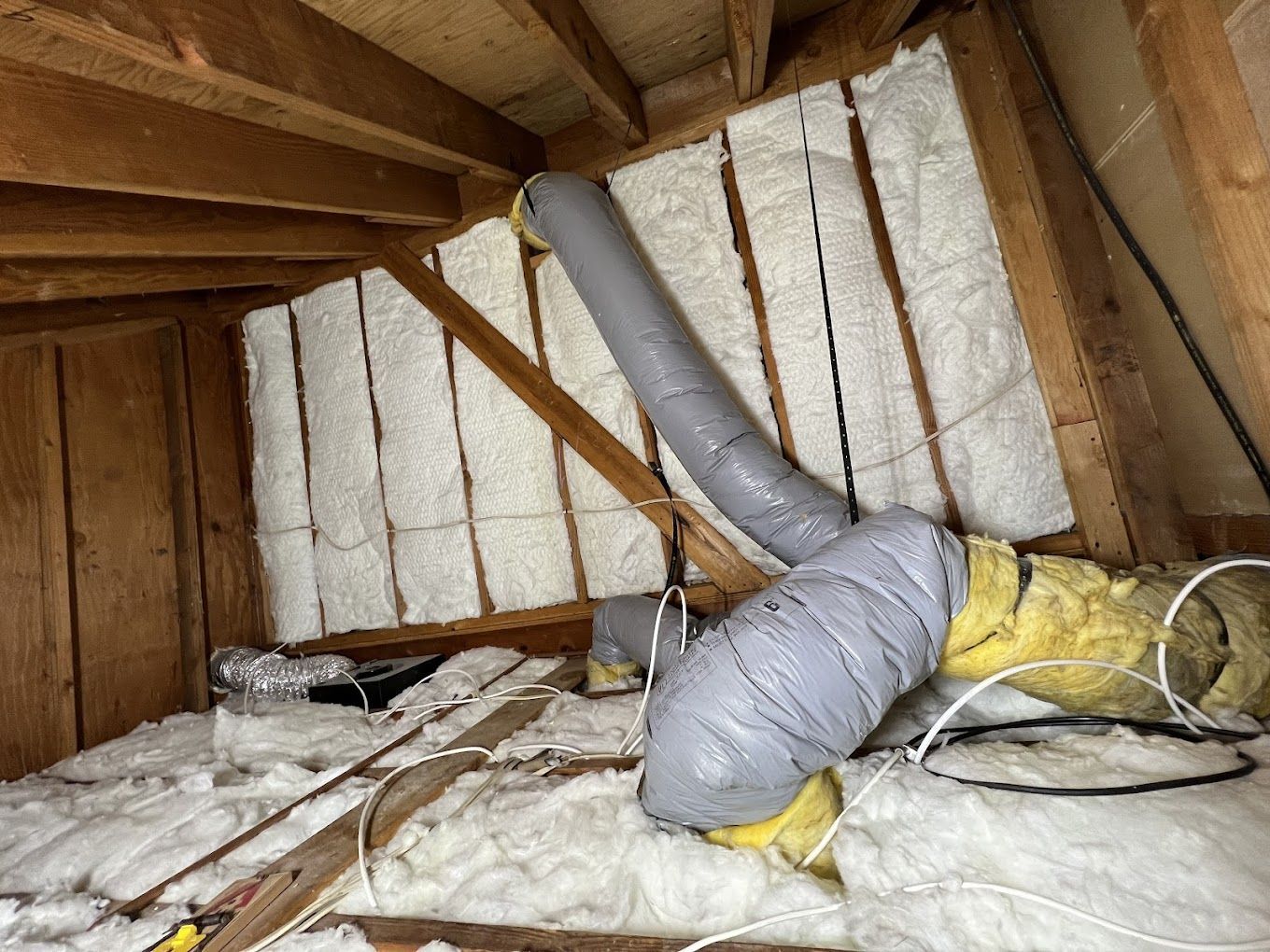 Attic with insulation and ductwork between wooden beams.