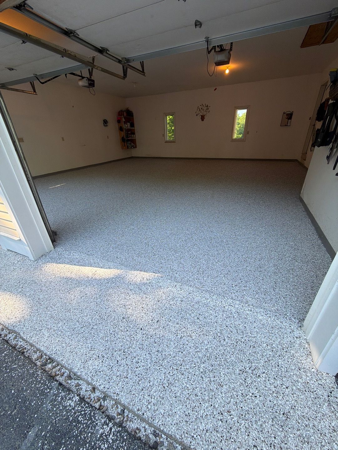 Empty garage with speckled epoxy floor, open door, and small windows.