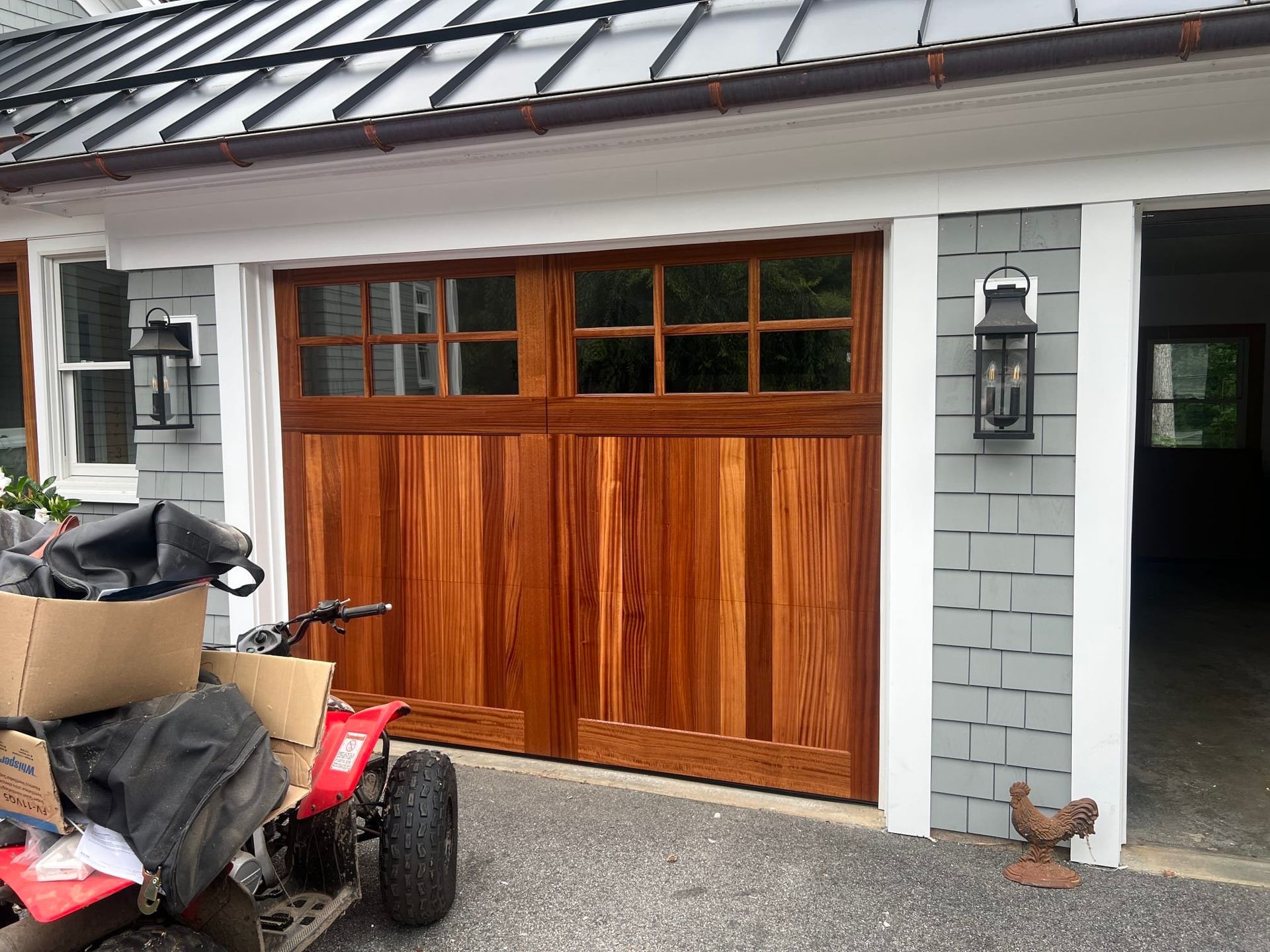 Wooden garage door beside gray brick wall, with an ATV parked in front and a doorway to the right.