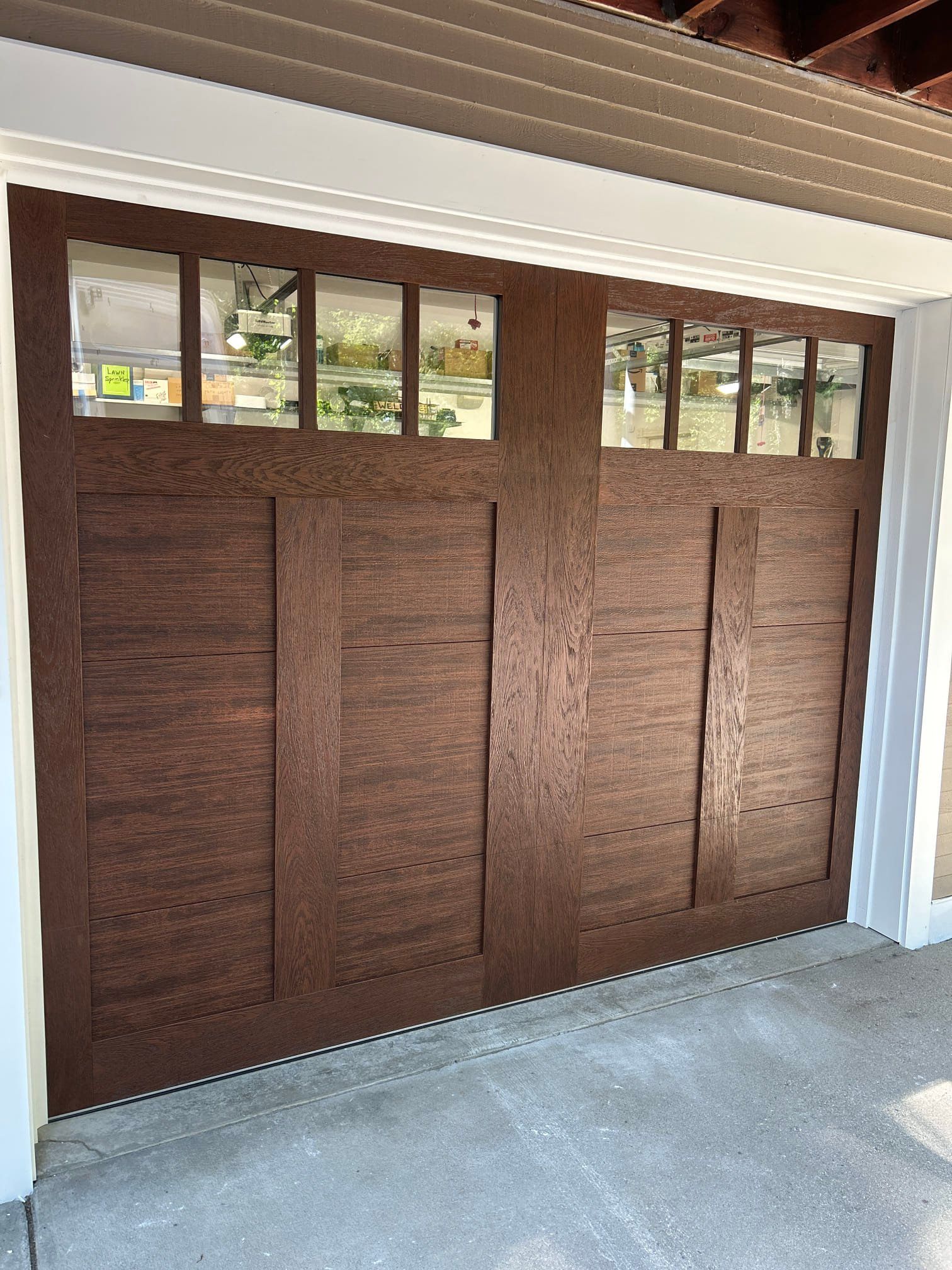 Brown wooden garage door with small windows along the top, viewed from outside under a covered porch