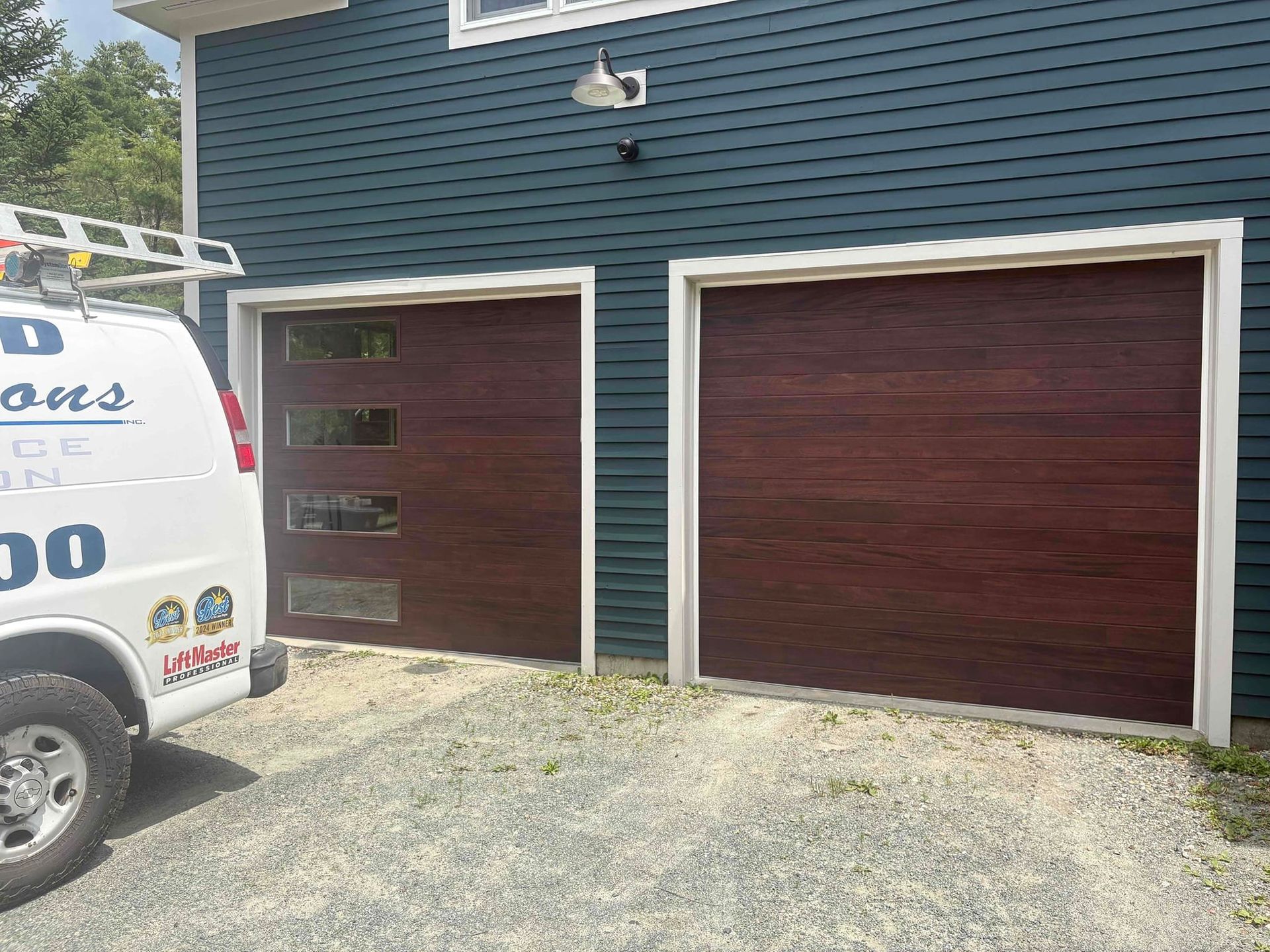 Two maroon garage doors on a blue-sided house, with a white work van partially visible on the left.