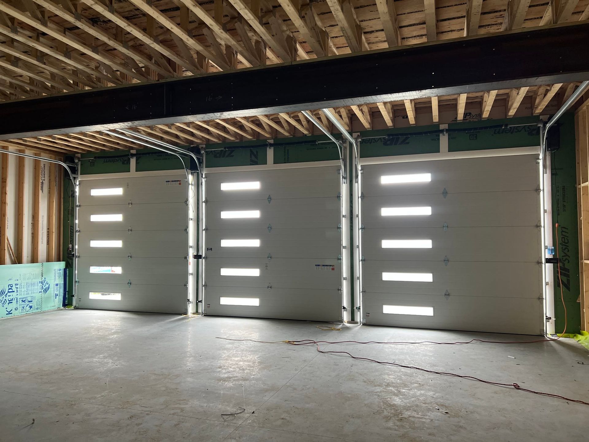 Three white garage doors with narrow windows in an unfinished indoor space.