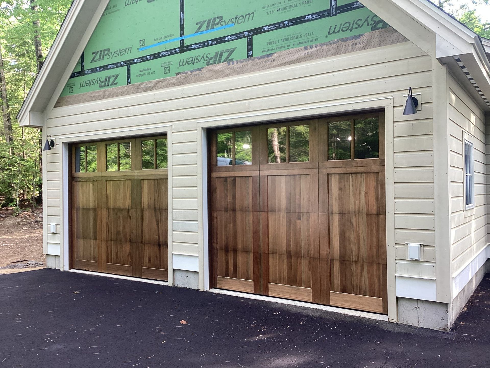 Two wooden garage doors on a white shed-like building with green trim and unfinished upper siding