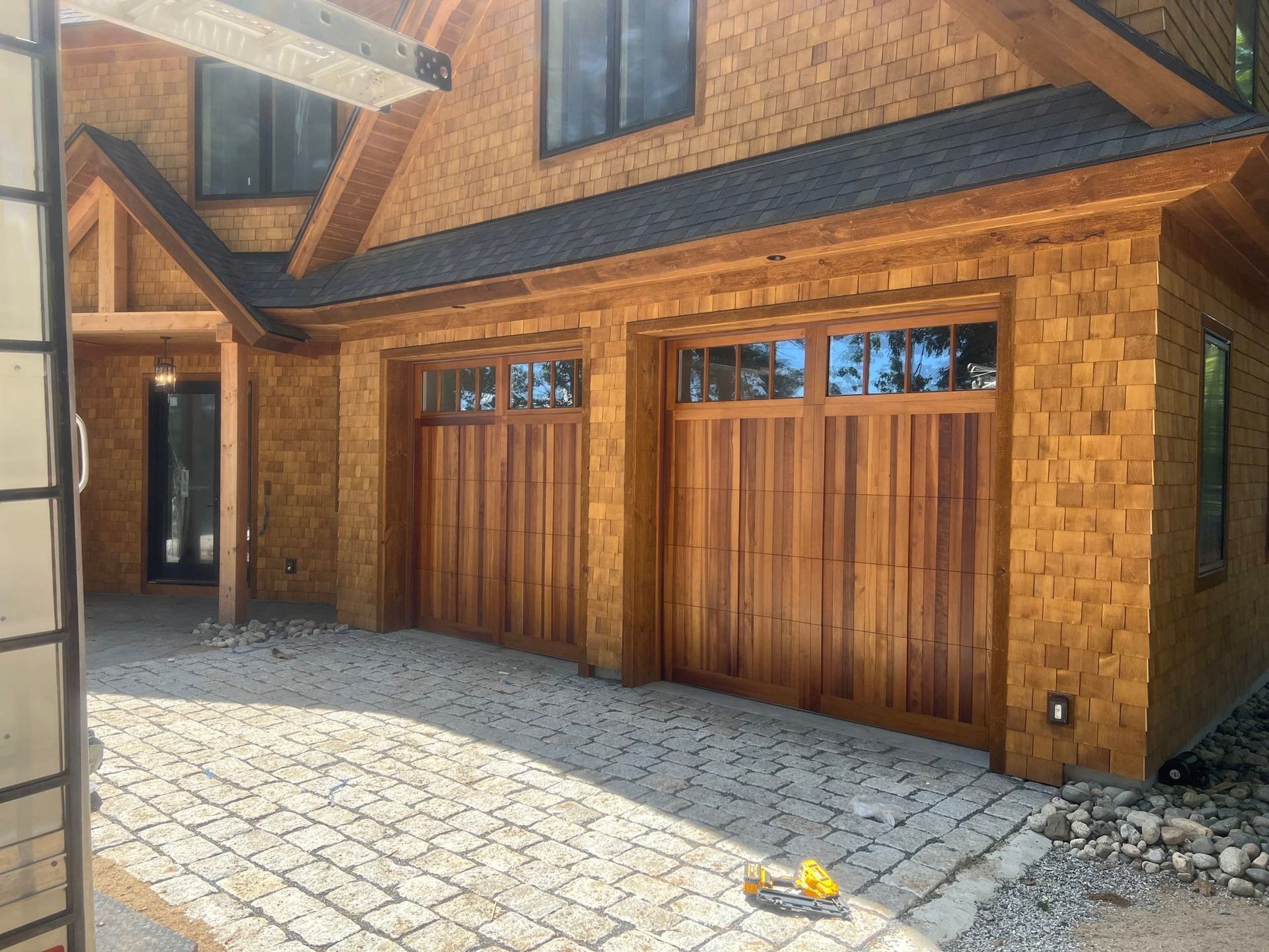 Wood-clad garage and entryway with cobblestone driveway and stone siding in warm daylight