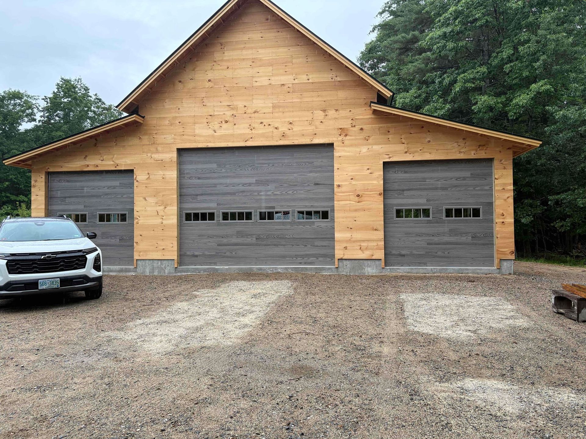 Wood-sided three-car garage with gray doors and a gravel driveway; white car parked at left.