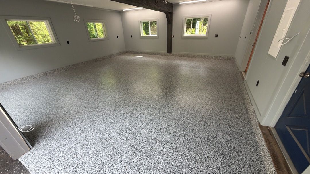 Empty gray garage with speckled floor, white walls, small windows, and a blue door.