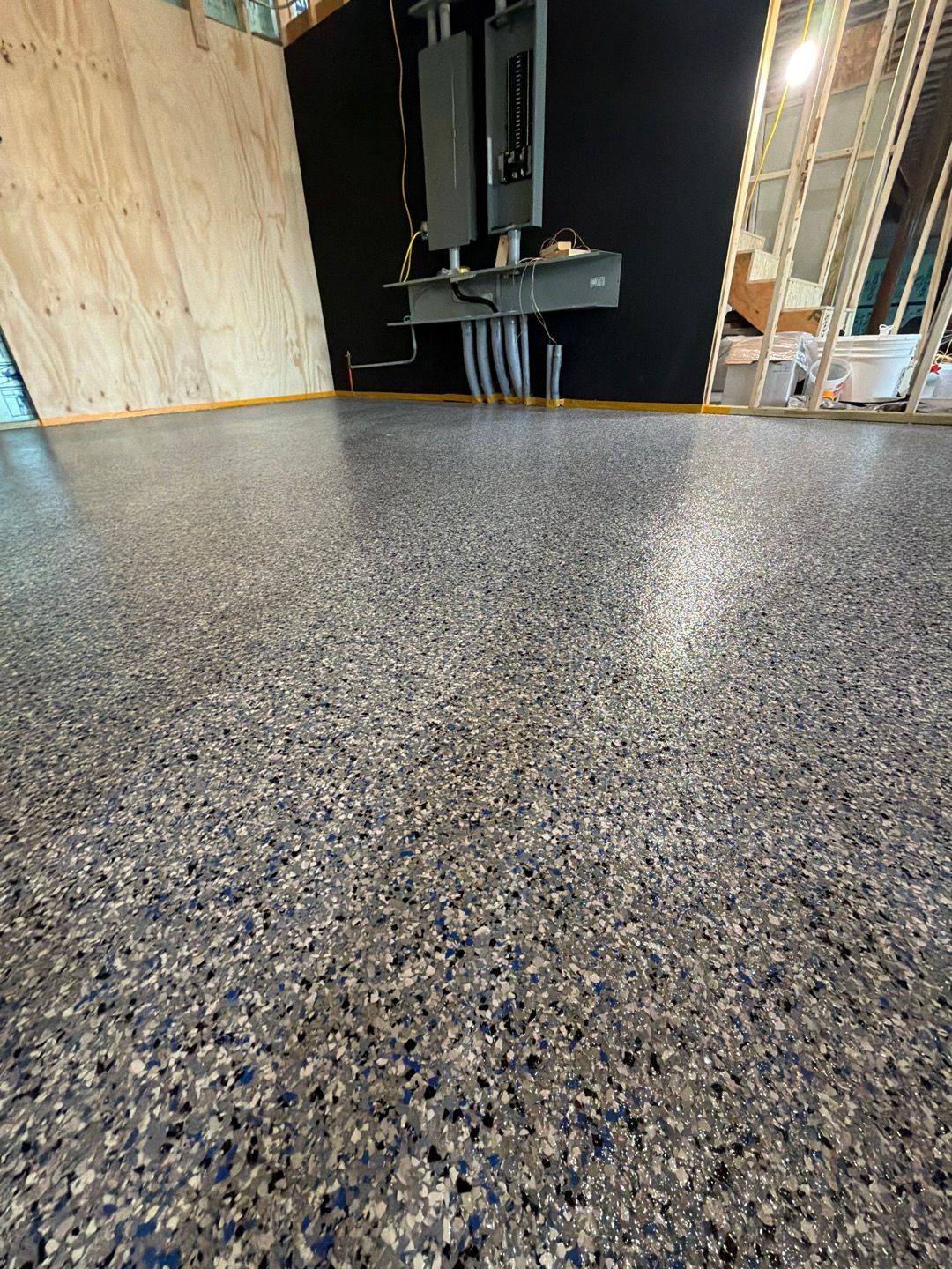 Speckled epoxy floor in an unfinished interior with plywood walls and a sink area.