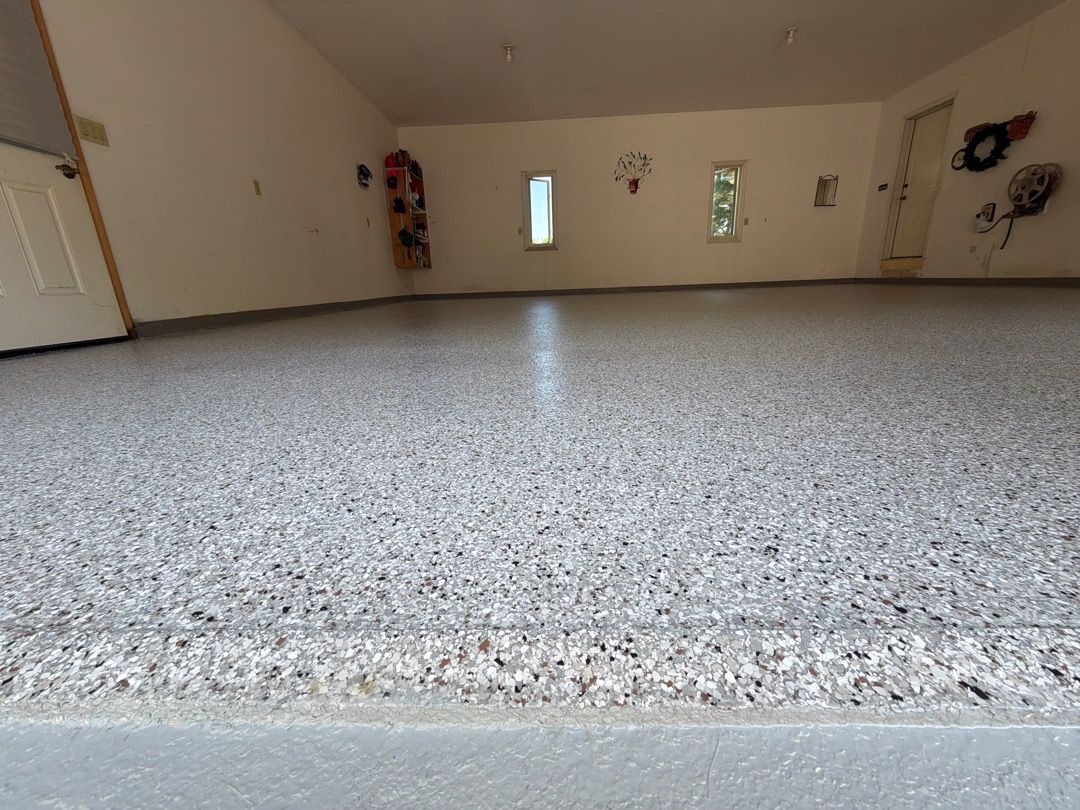 Empty garage with a speckled epoxy floor and beige walls, viewed from a low angle.
