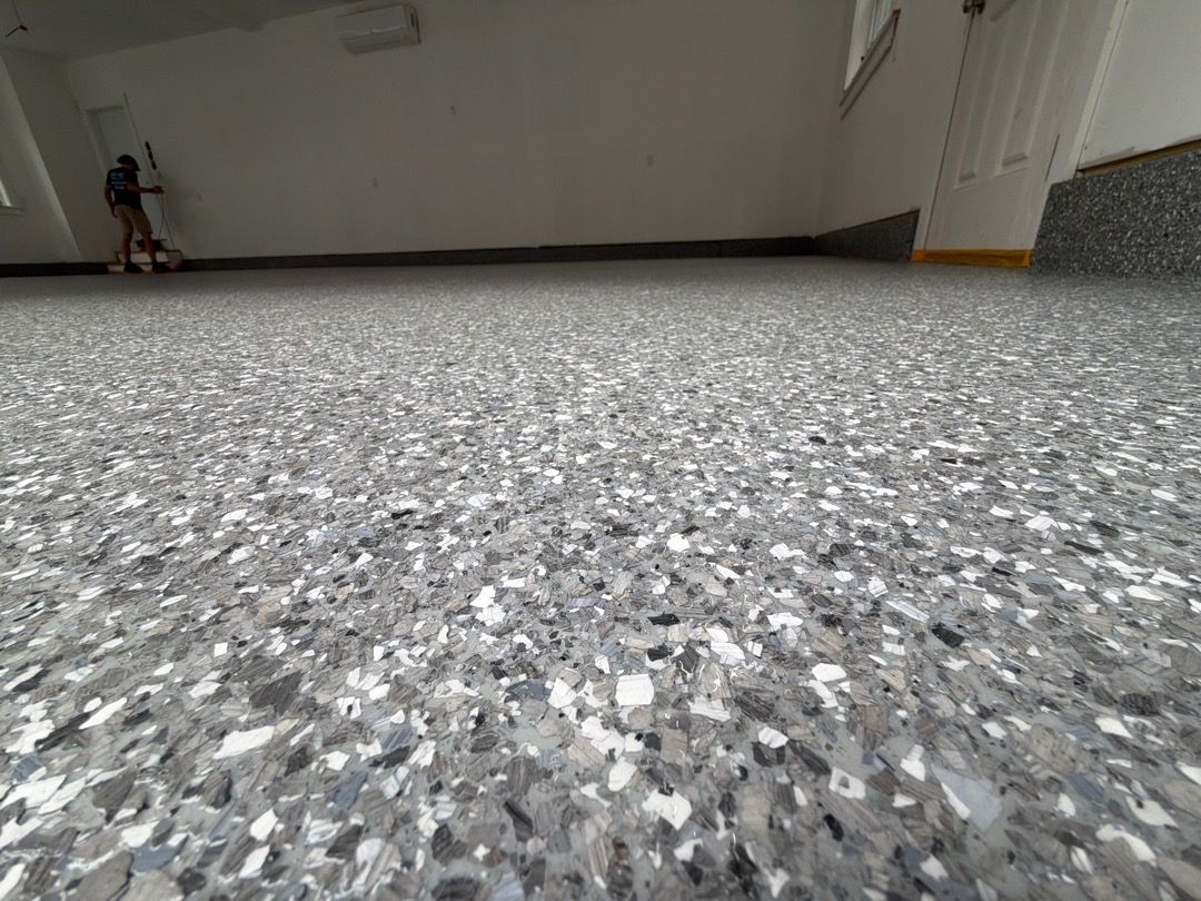 Low-angle view of a gray speckled floor in a sparse indoor room with a person sitting in the far left corner
