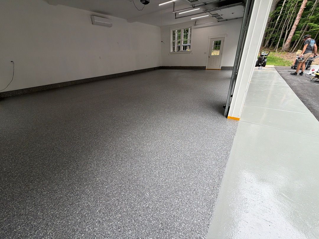 Empty garage interior with gray speckled floor and open doorway to outside.