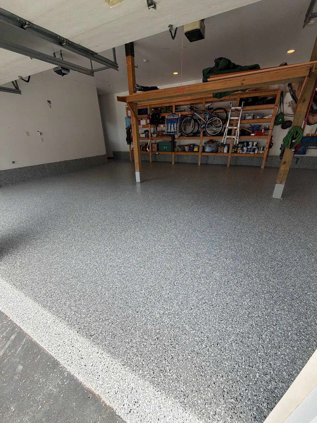 Empty garage with speckled gray floor and shelves along the back wall.