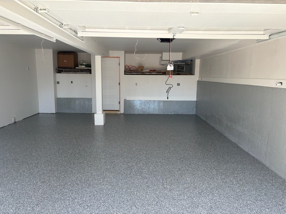 Empty garage with gray speckled floor, white walls, and a small back utility area.