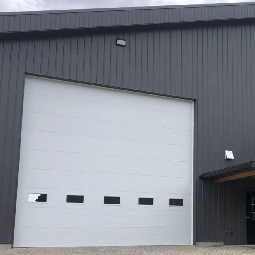 White garage door on a gray building with black trim, and a light above the door.