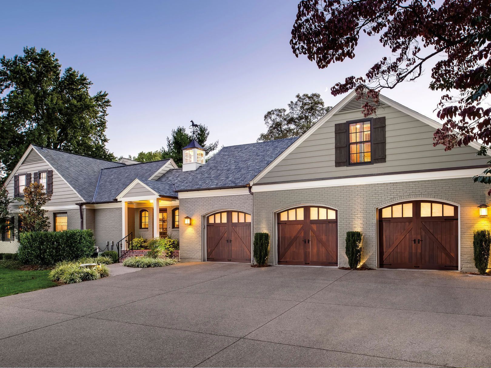 Tan brick home with three-car garage, brown doors, gray roof, and paved driveway.