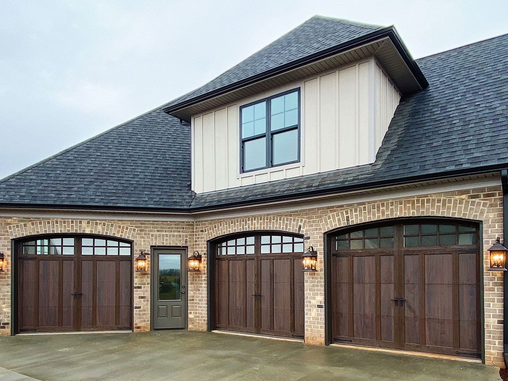 Three-car garage with brown doors, brick facade, and dormer window.
